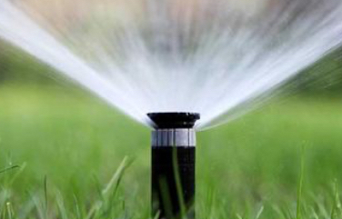 Closeup of a irrigation sprinkler spraying water on a green grass